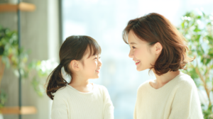 札幌の明るい歯科医院で、小児矯正の相談をして安心した表情で微笑み合う親子と温かい自然光の風景。