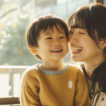 Smiling woman and young boy share a joyful moment by a sunlit window indoors.