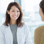 Smiling female clinician in a white coat speaks with a patient in a bright, modern clinic.