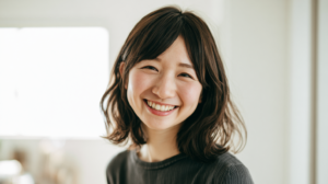 Young woman with shoulder-length dark hair smiles warmly indoors, wearing a dark knit sweater.