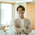 Smiling man in a light blazer, arms crossed, standing in a bright office or clinic lobby.”