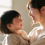 Mother holds smiling toddler in a sunlit room, facing each other with joy in warm light.