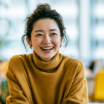明るいオフィスで周囲の目を気にせず、笑顔で自然に会話を楽しむ大人の女性（マウスピース矯正のイメージ）