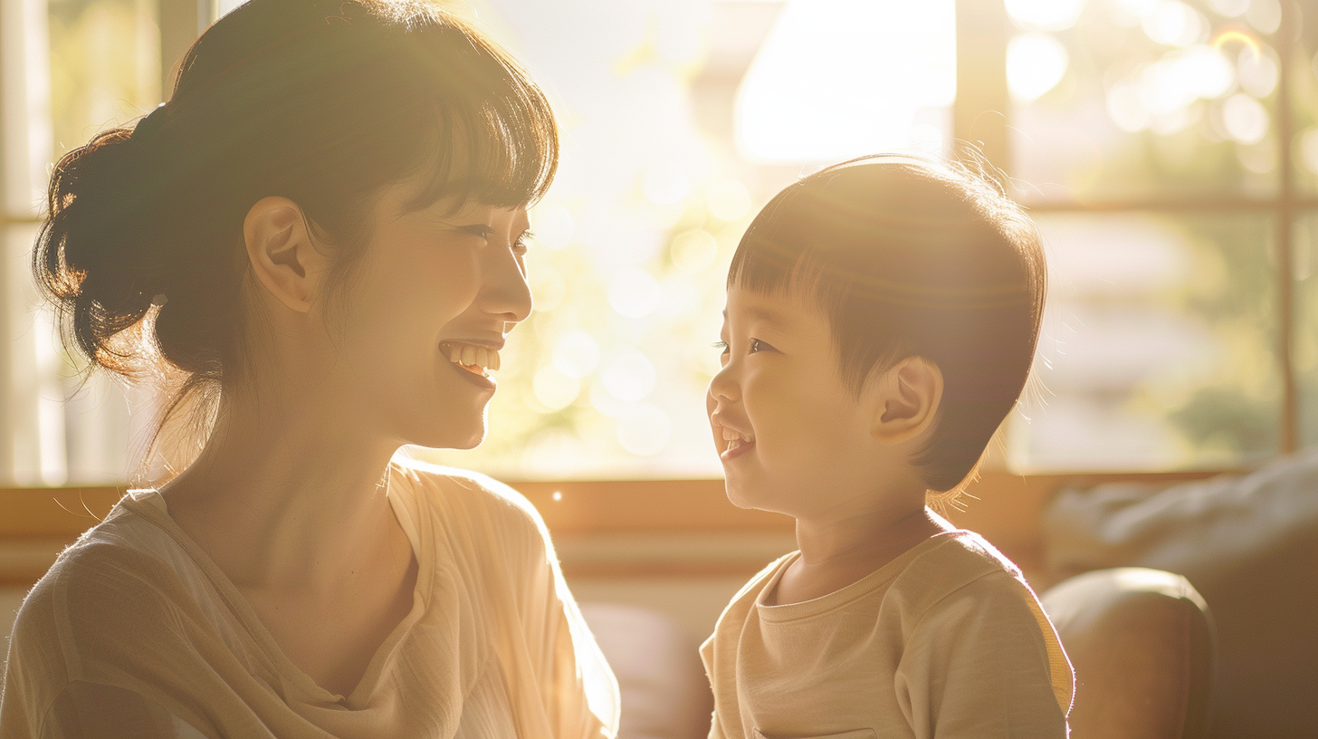 自然光の入る明るい部屋で、笑顔で見つめ合う親子の様子（小児矯正の相談）
