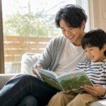 明るい部屋で一緒に絵本を読む父親と子ども